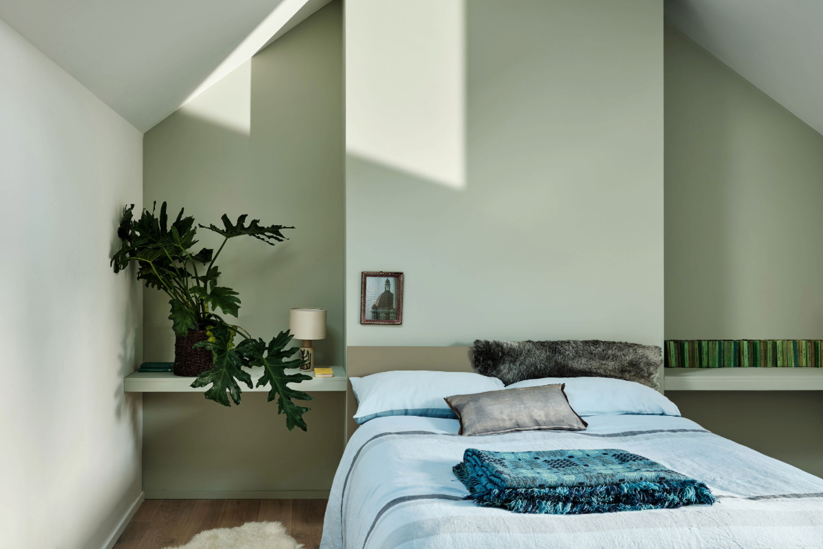 A bedroom painted in pale green with a bed and plant